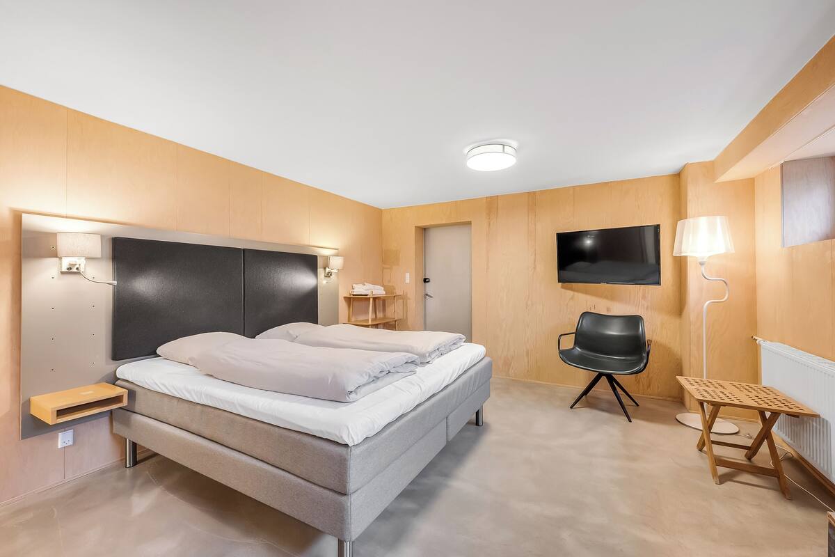 Una habitación de hotel moderna con una cama grande, mesitas de noche, un escritorio, una silla y un televisor montado en la pared.
