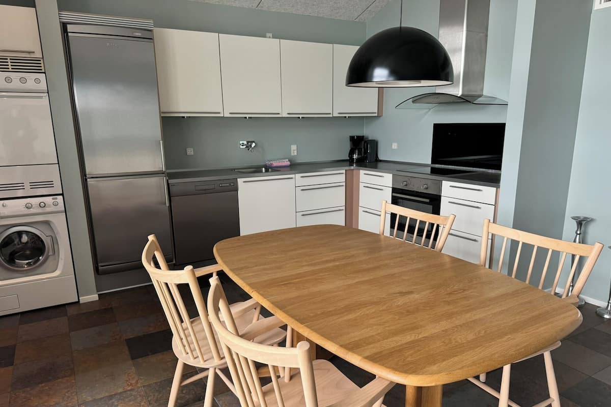 Una cocina moderna con zona de comedor. Incluye un refrigerador de acero inoxidable, lavavajillas, horno y lavadora. Hay una mesa de comedor de madera con cuatro sillas.