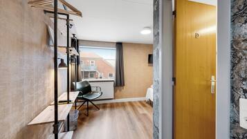 Una habitación moderna con suelo de madera, una silla negra, un escritorio y un ventanal con vistas a edificios.