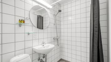 A bathroom with white tiled walls, a white sink, a mirror, a shower, and a toilet.