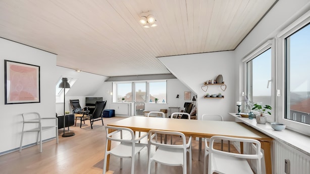 Une pièce spacieuse avec une grande table en bois, des chaises blanches et une vue dégagée grâce à de grandes fenêtres.