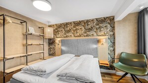 Une chambre d’hôtel moderne avec un lit, un fauteuil vert et une étagère.