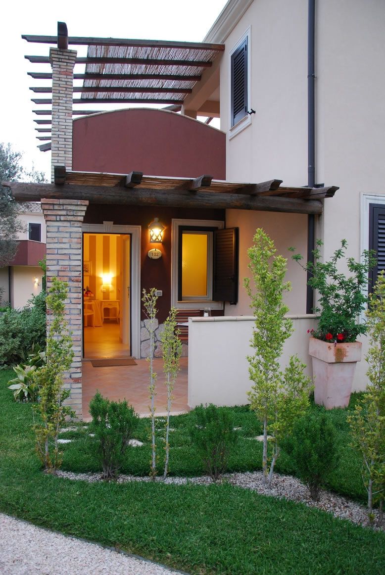 Une maison moderne dotée d’un porche abrité, d’une porte bien visible et d’un petit jardin avec de jeunes arbres.