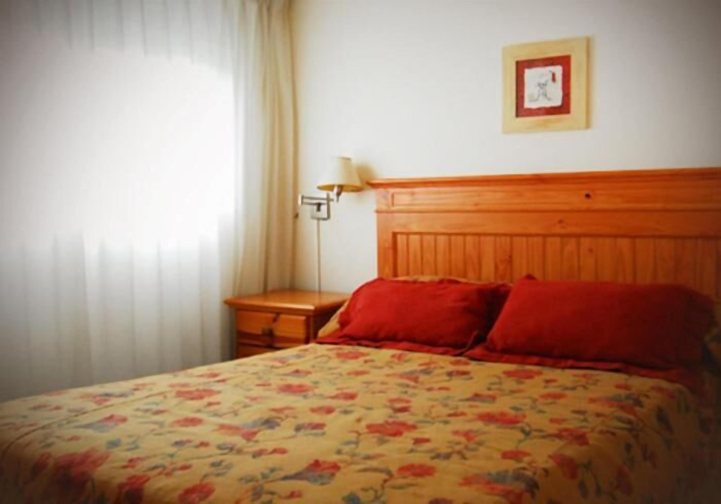A bedroom with a wooden headboard, a floral bedspread, and a nightstand with a lamp.