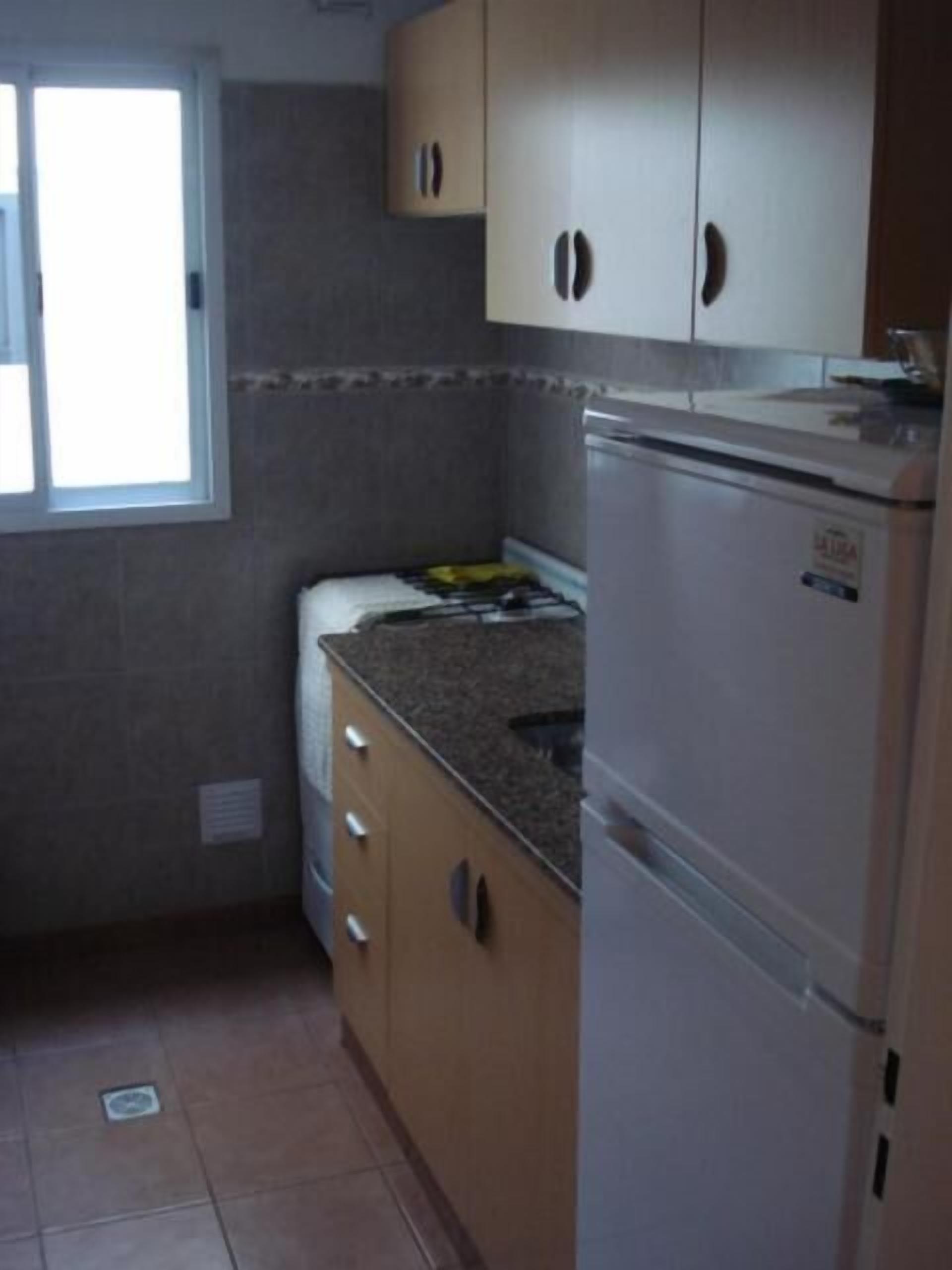 A compact kitchen with a refrigerator, a sink, and cabinets.