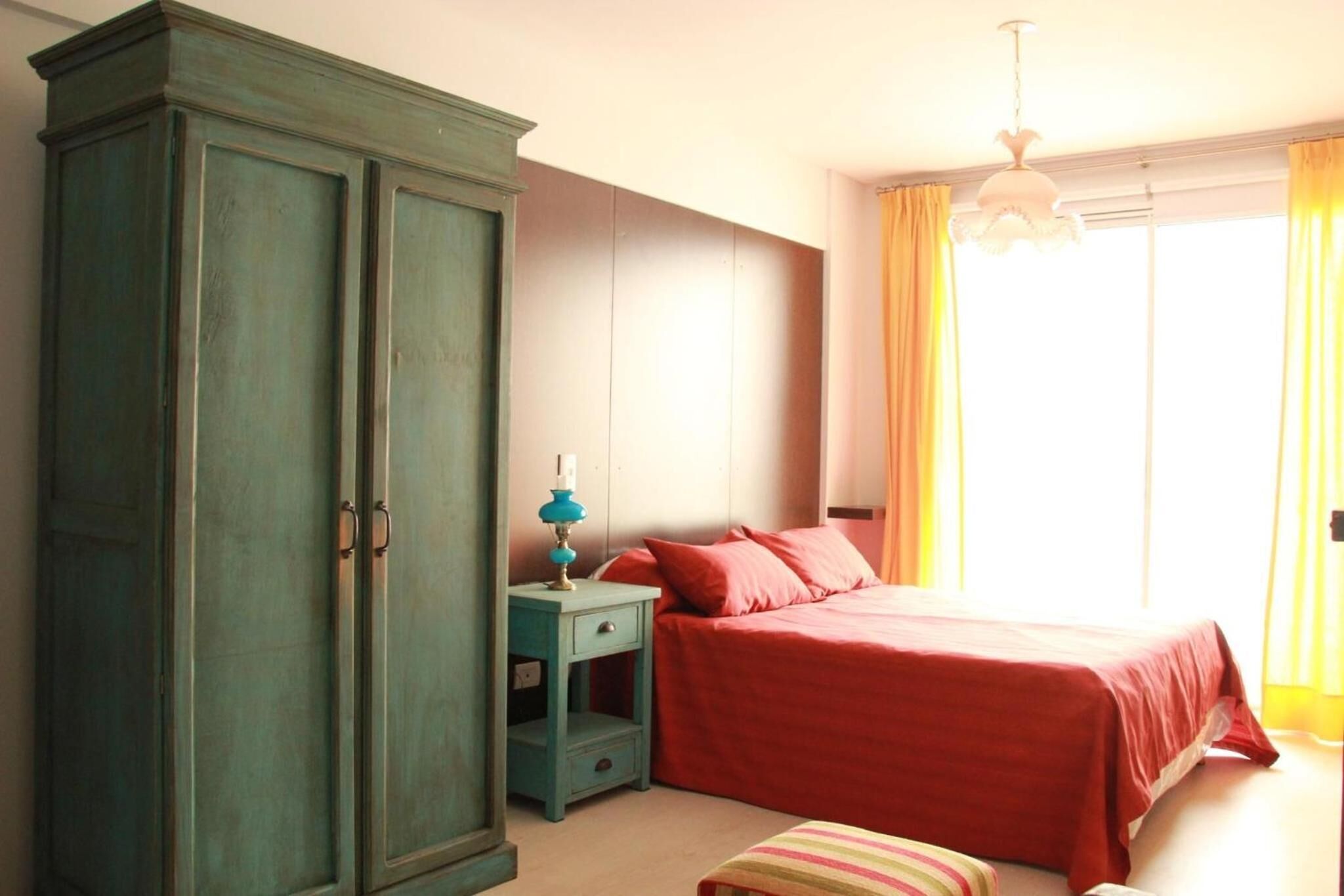 Une chambre à coucher comprenant un lit, une armoire, une table de chevet et une fenêtre avec des rideaux.