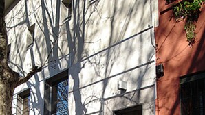 Un bâtiment à la façade de marbre, un arbre projetant des ombres et un mur rouge avec une fenêtre.