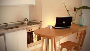 Une petite cuisine avec un évier, une cuisinière et un ordinateur portable posé sur une table en bois.