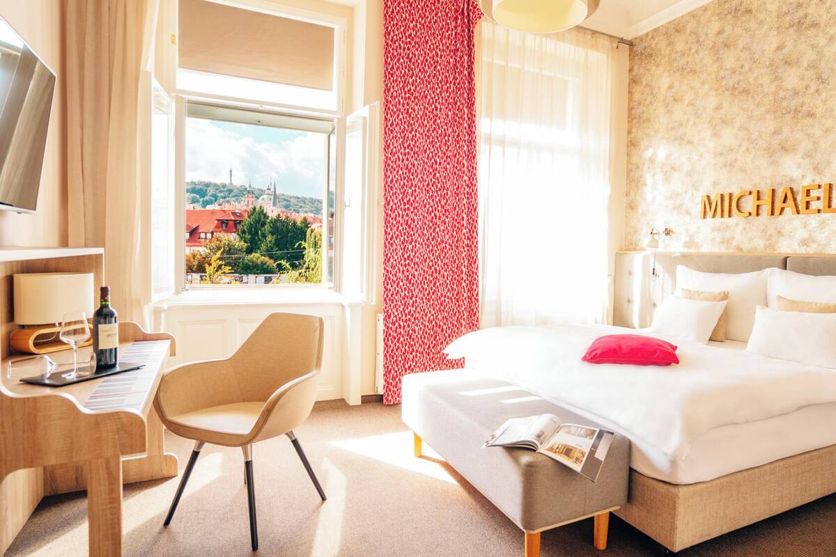 Hotelkamer met een bed, bureau, stoel, televisie en raam met uitzicht op gebouwen.