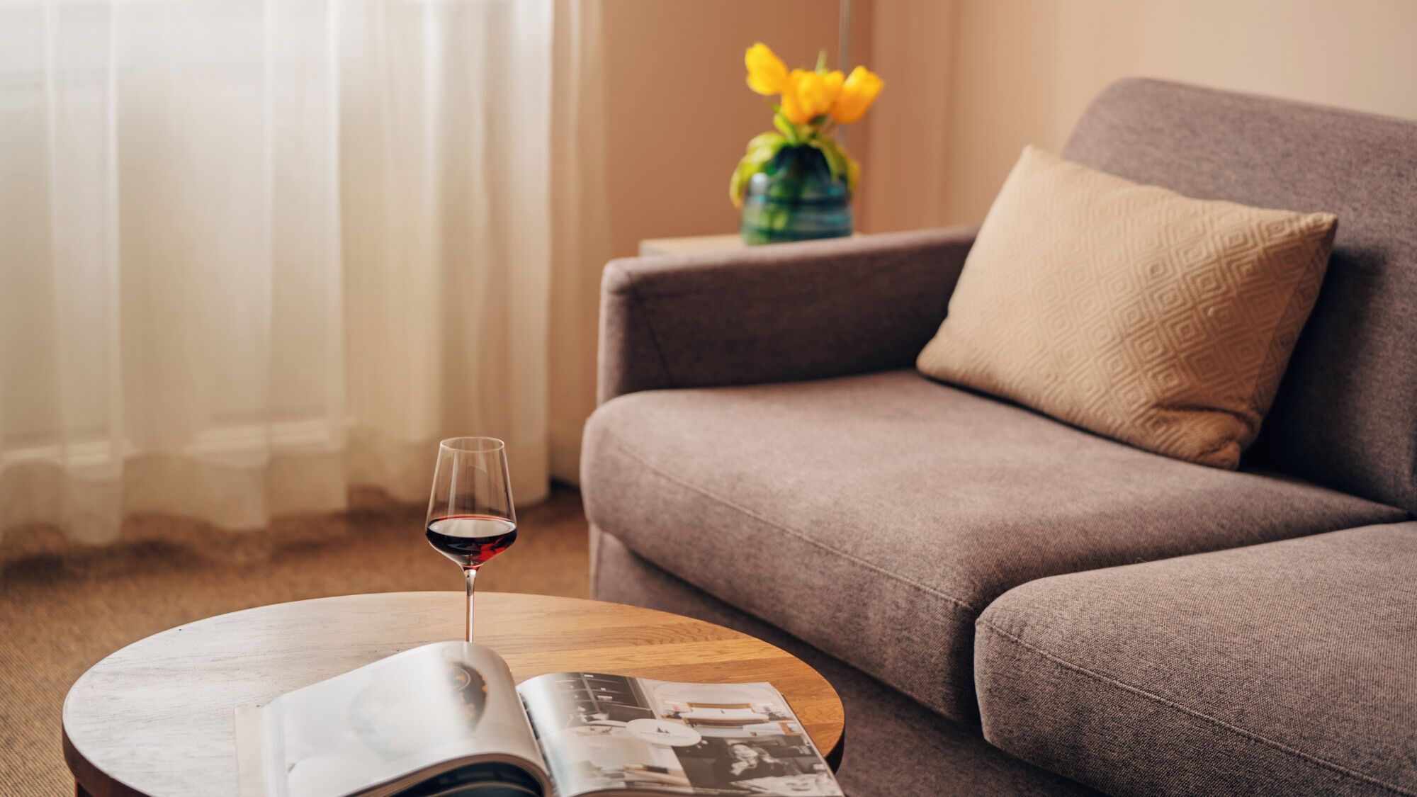 Una sala de estar con un sofá, una mesa de centro, una copa de vino tinto y una revista.