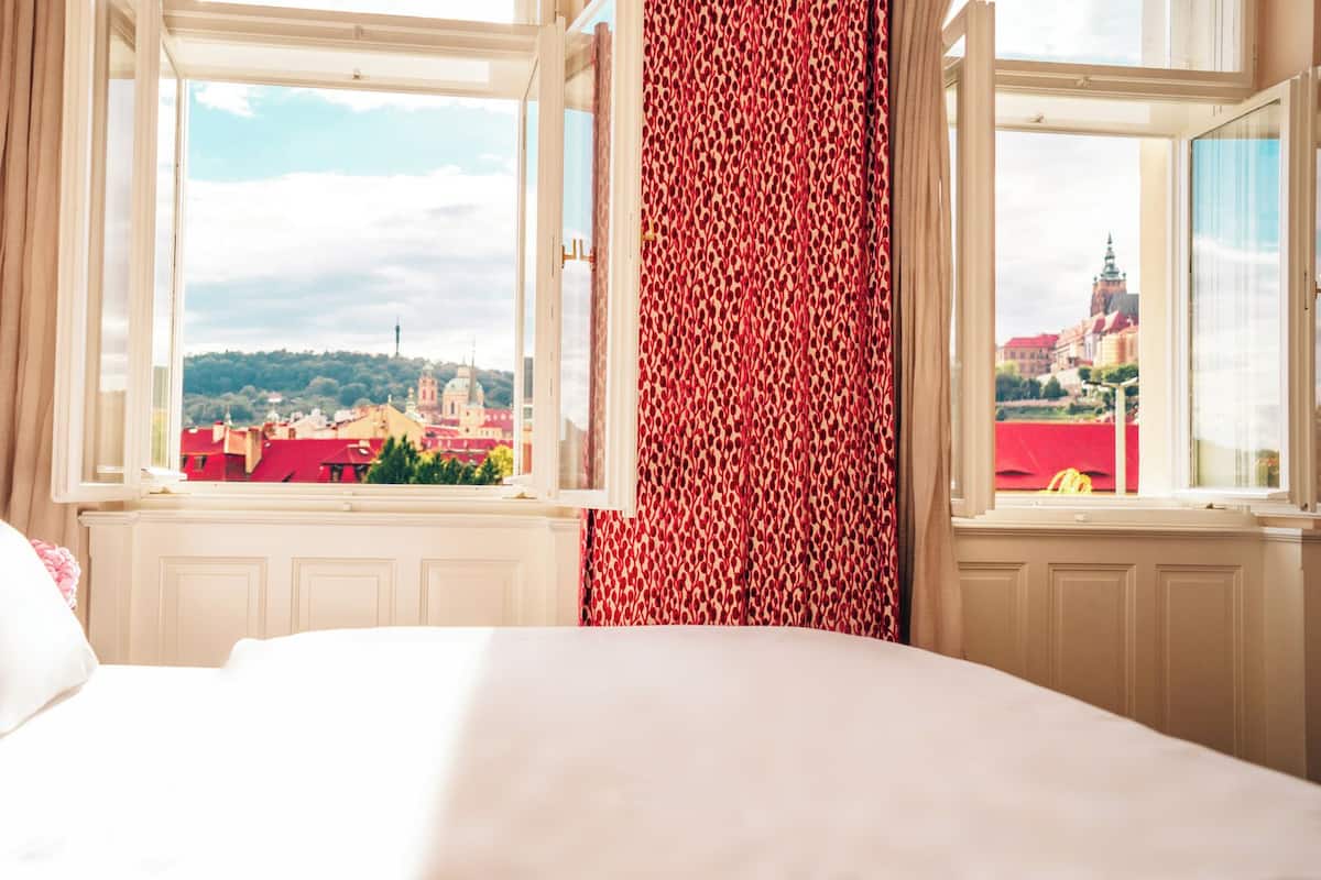 Een hotelkamer met een bed, een raam met uitzicht op een stadsgezicht en een kamer met een patroon gordijn.