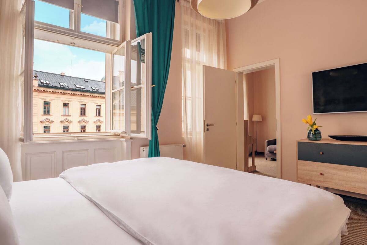 Een hotelkamer met een groot bed, een televisie, een houten dressoir en een raam met gordijnen.