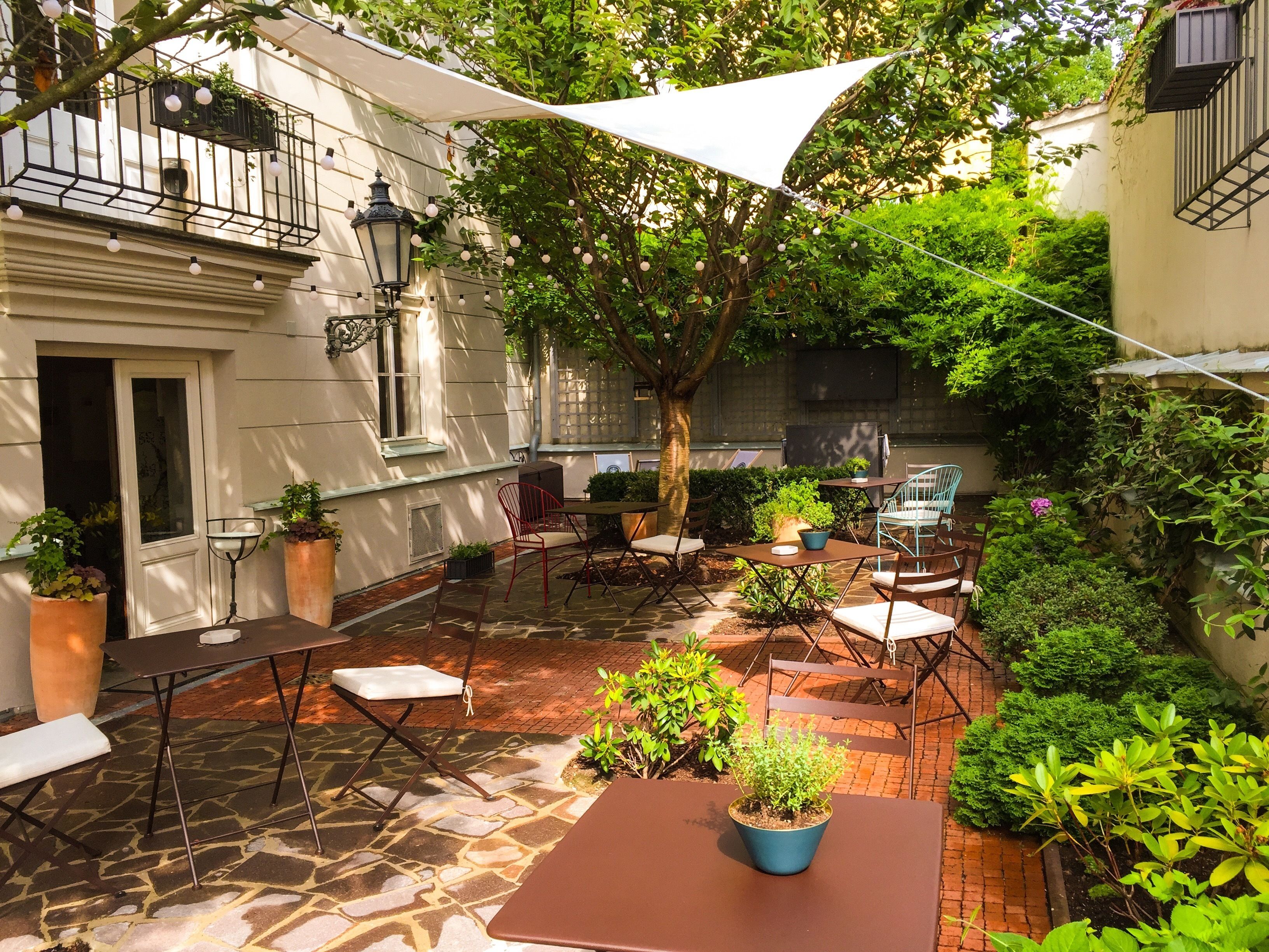 An outdoor patio area with stone flooring, tables, chairs, potted plants, and a white canopy.
