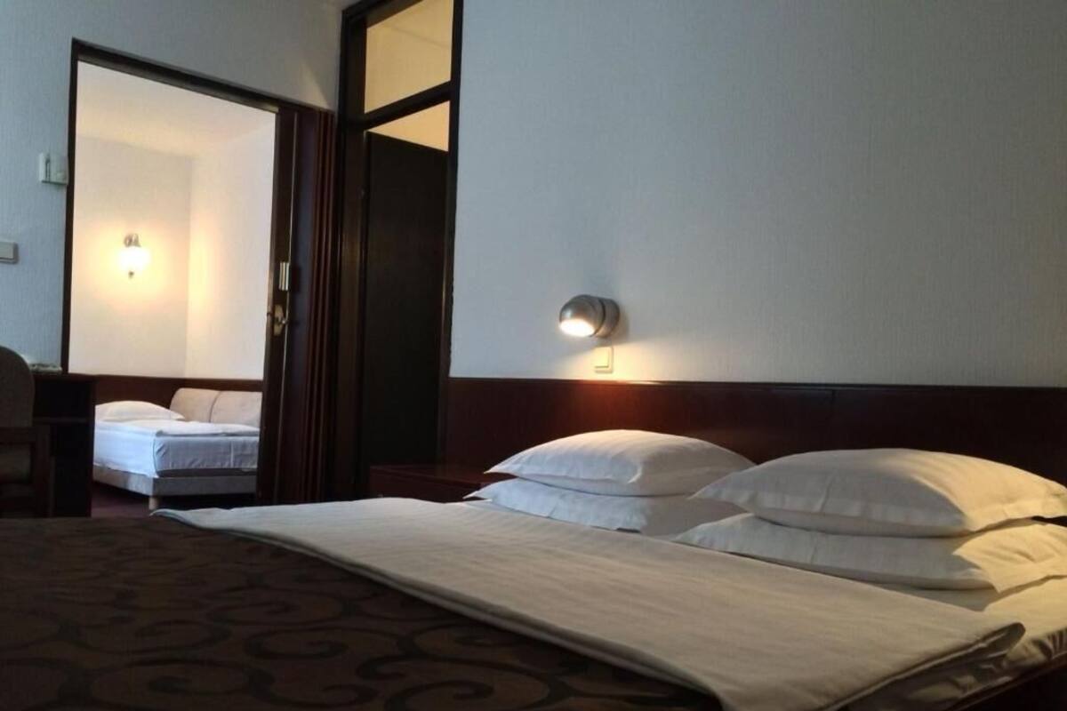A hotel room with a bed, a nightstand, a wall-mounted light, and a mirror.
