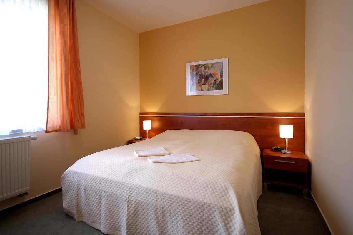 Ett hotellrum med en stor säng, två sänglampor, ett inramat konstverk på väggen och ett fönster med gardiner.