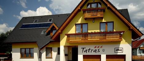 A two-story building with a yellow facade, a balcony with wooden railings, and a sign that reads "Tatra's".