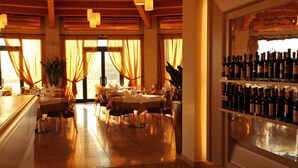 A restaurant with a wooden ceiling, large windows with curtains, and a wine rack filled with bottles. - Grand Hotel Forlì (Forlì)