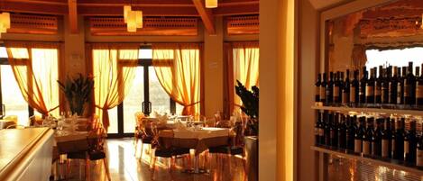 Un restaurante con techo de madera, ventanas amplias con cortinas y una estantería llena de botellas de vino.
