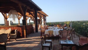 An outdoor dining area with tables and chairs, a bar, and a view of the landscape. - Grand Hotel Forlì (Forlì)