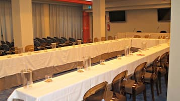 Un salón de conferencias con mesas largas, sillas y un extintor en la pared.