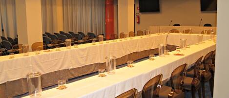 Un salón de conferencias con mesas largas, sillas y un extintor en la pared.