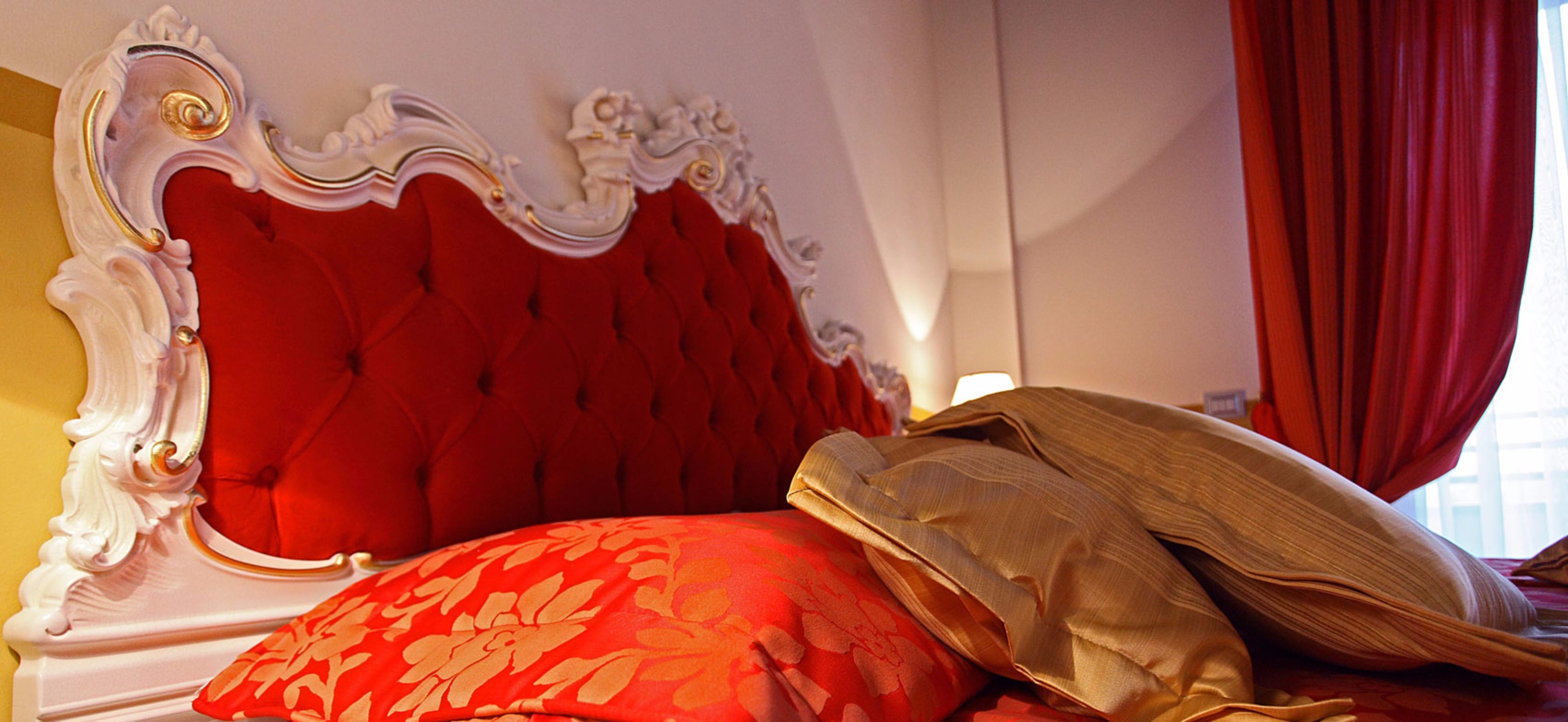 Un lit avec une tête de lit rembourrée de tissu rouge et des oreillers à motifs floraux.