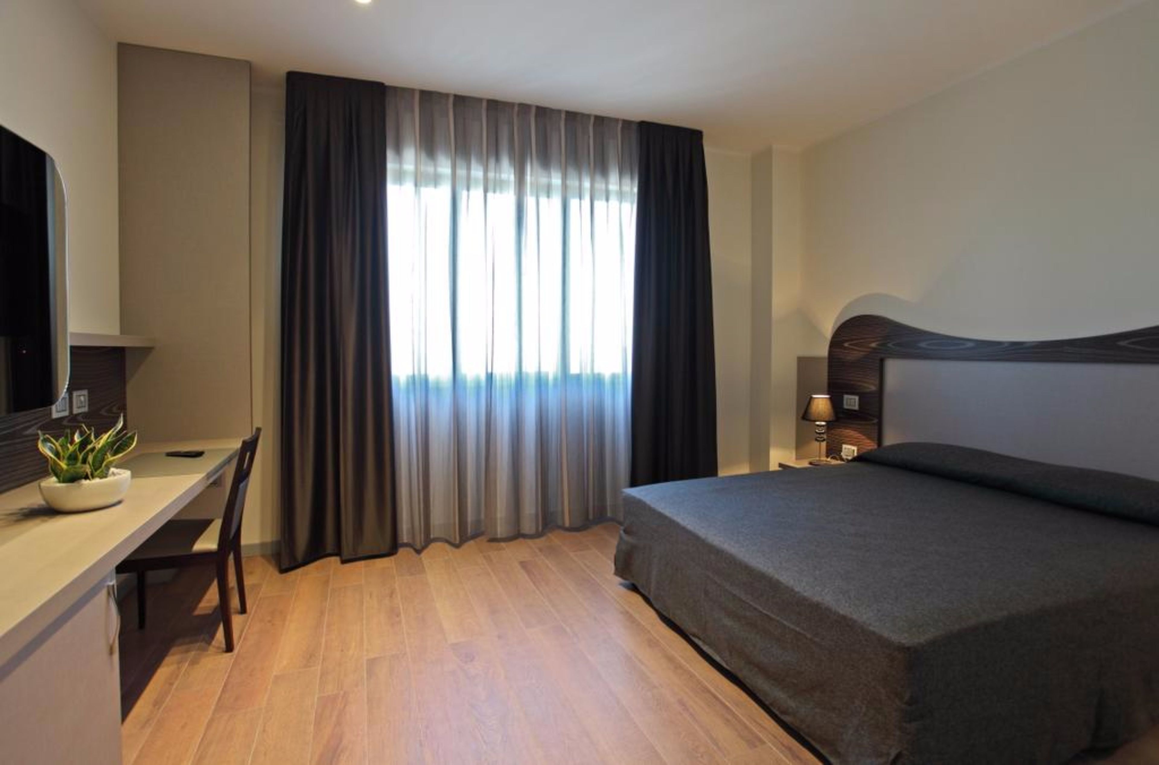 A modern hotel room with a bed, a desk, and a TV.