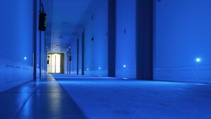 A long, narrow hallway with a blue hue, leading to a bright doorway at the end. - Grand Hotel Forlì (Forlì)