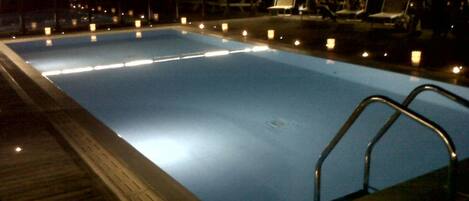 Ein Schwimmbad bei Nacht mit Lichtern und Liegestühlen im Hintergrund.