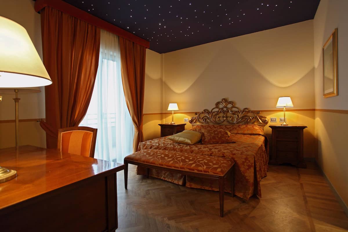 A bedroom with a starry ceiling, a bed with a floral bedspread, two bedside tables with lamps, and a wooden desk with a lamp.