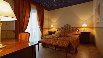 A bedroom with a starry ceiling, a bed with a floral bedspread, two bedside tables with lamps, and a wooden desk with a lamp.