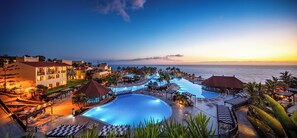 Un resort con múltiples piscinas, áreas de descanso y vistas a la playa.
