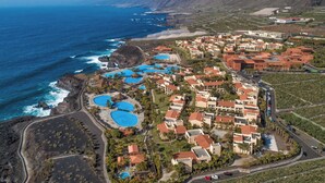 An aerial view of a coastal resort with multiple swimming pools, beachfront villas, and a mountainous backdrop. - Hotel La Palma Princess (Fuencaliente de la Palma)