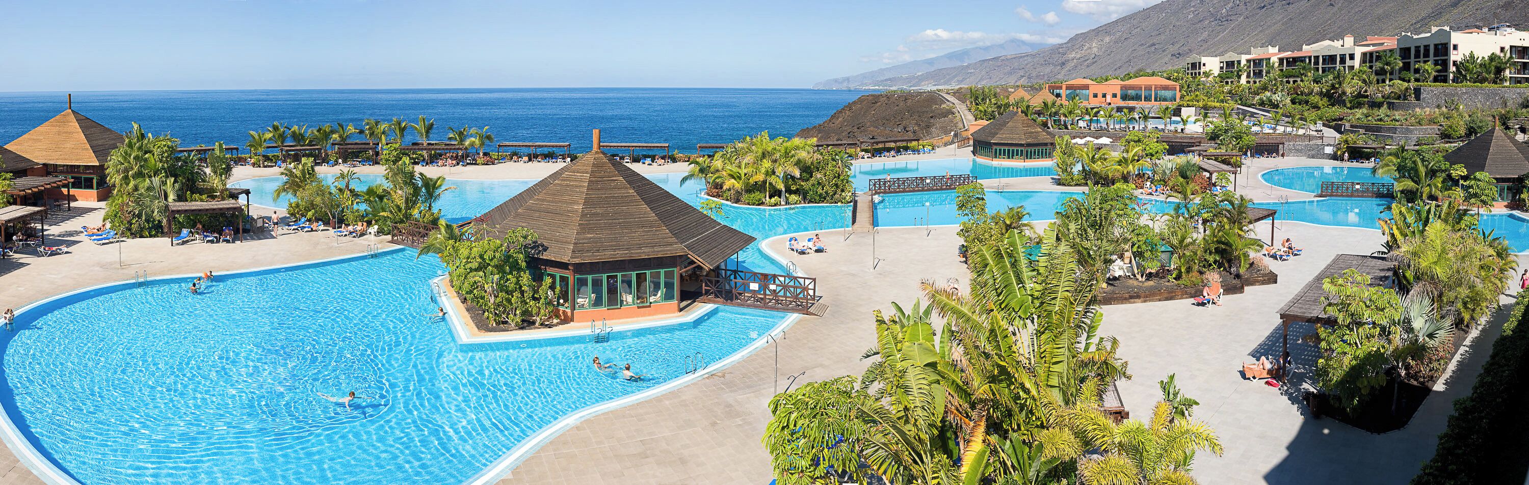 A resort with multiple swimming pools, a beach, and a mountainous backdrop.