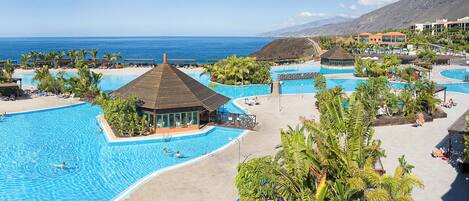 A resort with multiple swimming pools, a beach, and a mountainous backdrop.