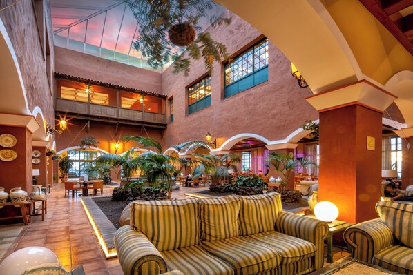 A spacious lobby with a high ceiling, multiple seating areas, and a central plant arrangement. - Hotel La Palma Princess (Fuencaliente de la Palma)