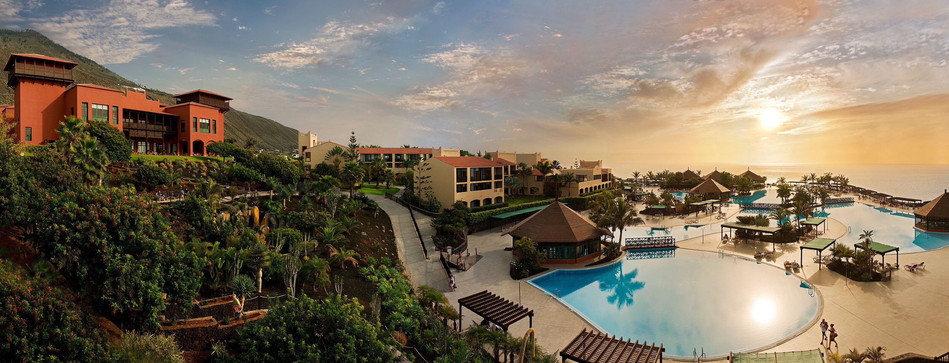 Un resort con una gran piscina, varias construcciones y montañas al fondo.