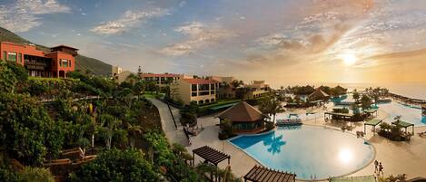 Un resort con una gran piscina, varias construcciones y montañas al fondo.