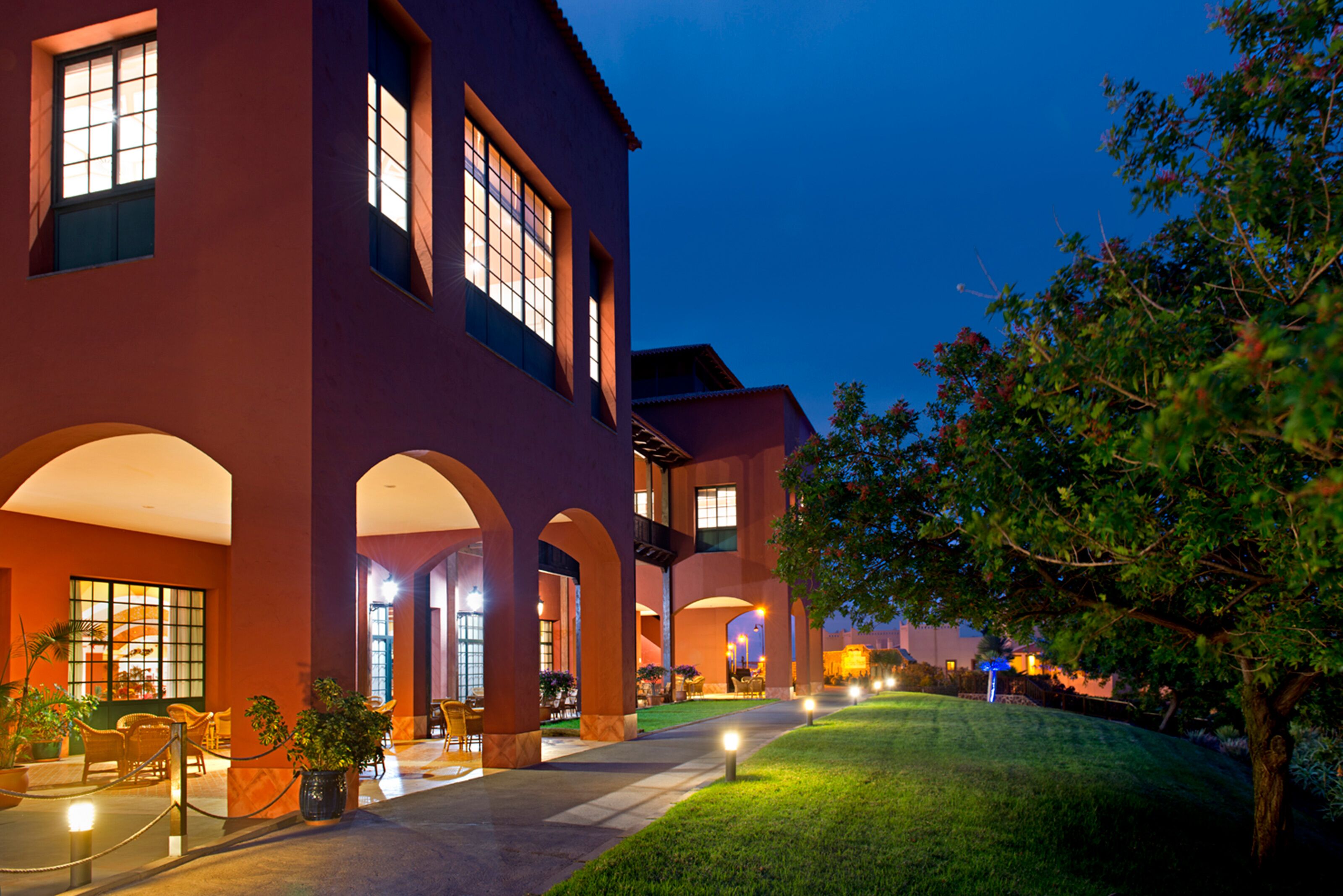 A building with multiple arches and large windows, a well-maintained lawn, and potted plants.