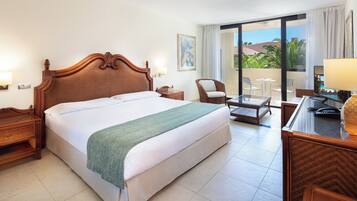Habitación de hotel con una cama grande, una silla, un escritorio y un balcón con vistas a palmeras.