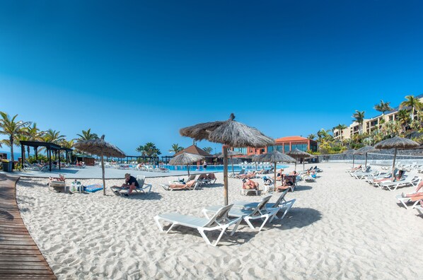 Una playa con tumbonas, sombrillas y una zona de piscina.