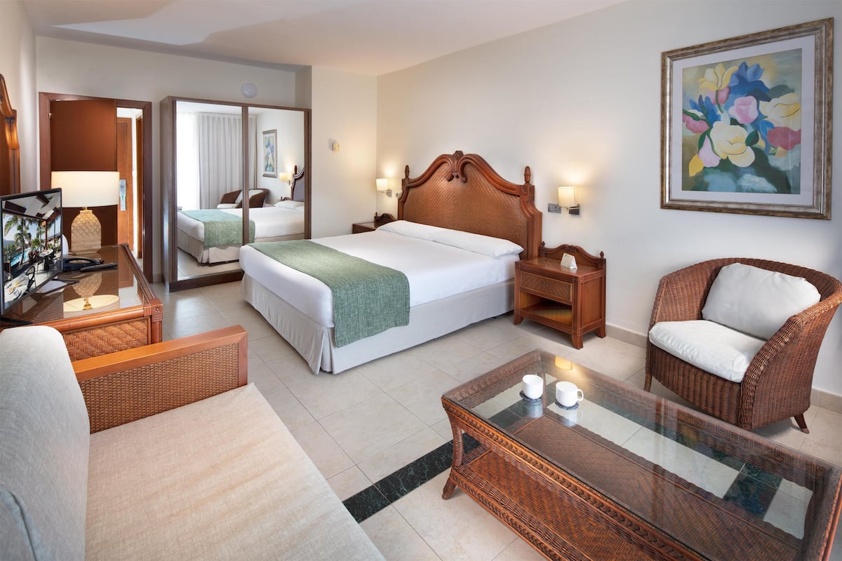 Une chambre d’hôtel dotée d’un grand lit, d’un coin salon avec un canapé et un fauteuil, d’une table basse en verre et d’un tableau au mur.