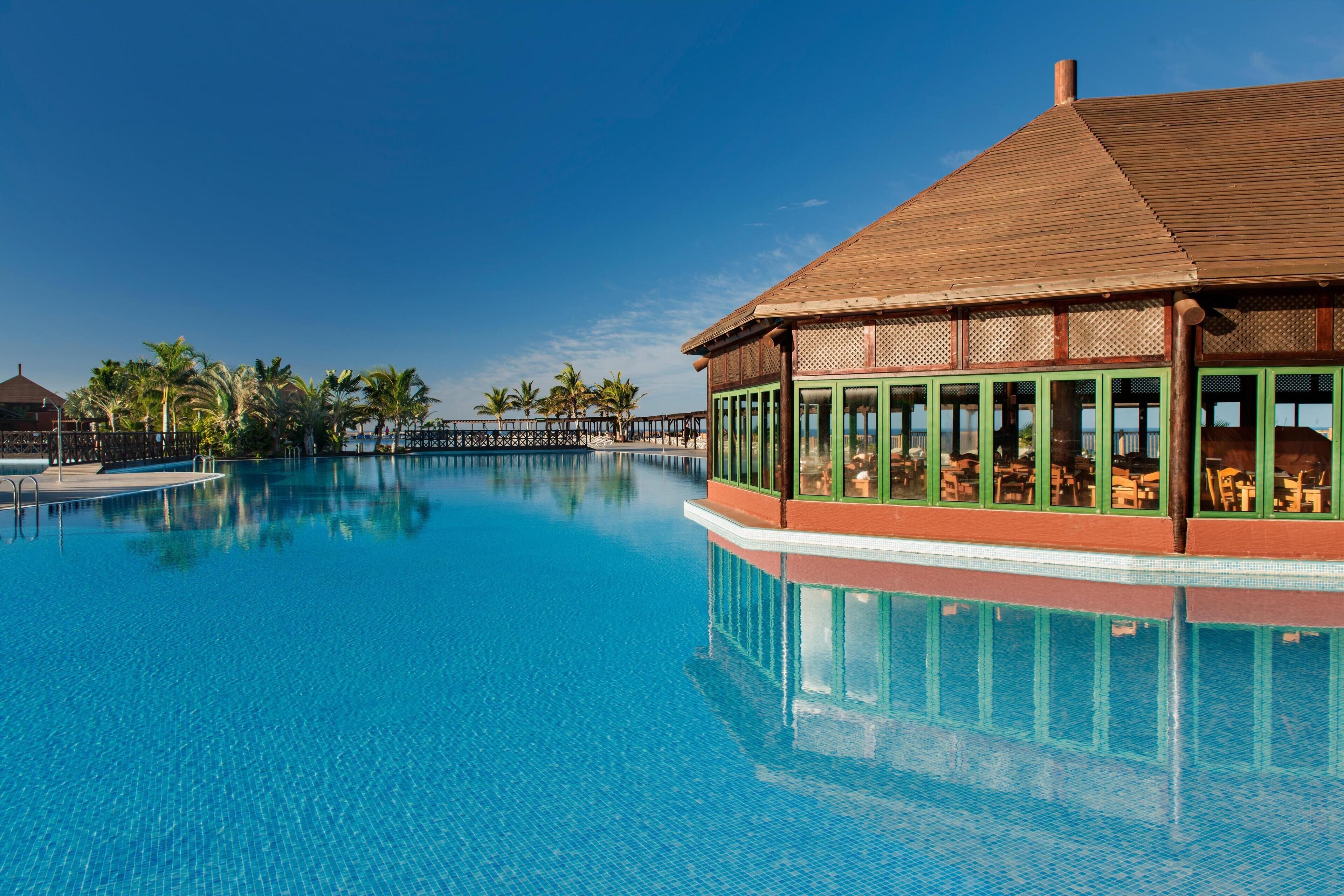 A large, clear swimming pool with a wooden structure on one side.