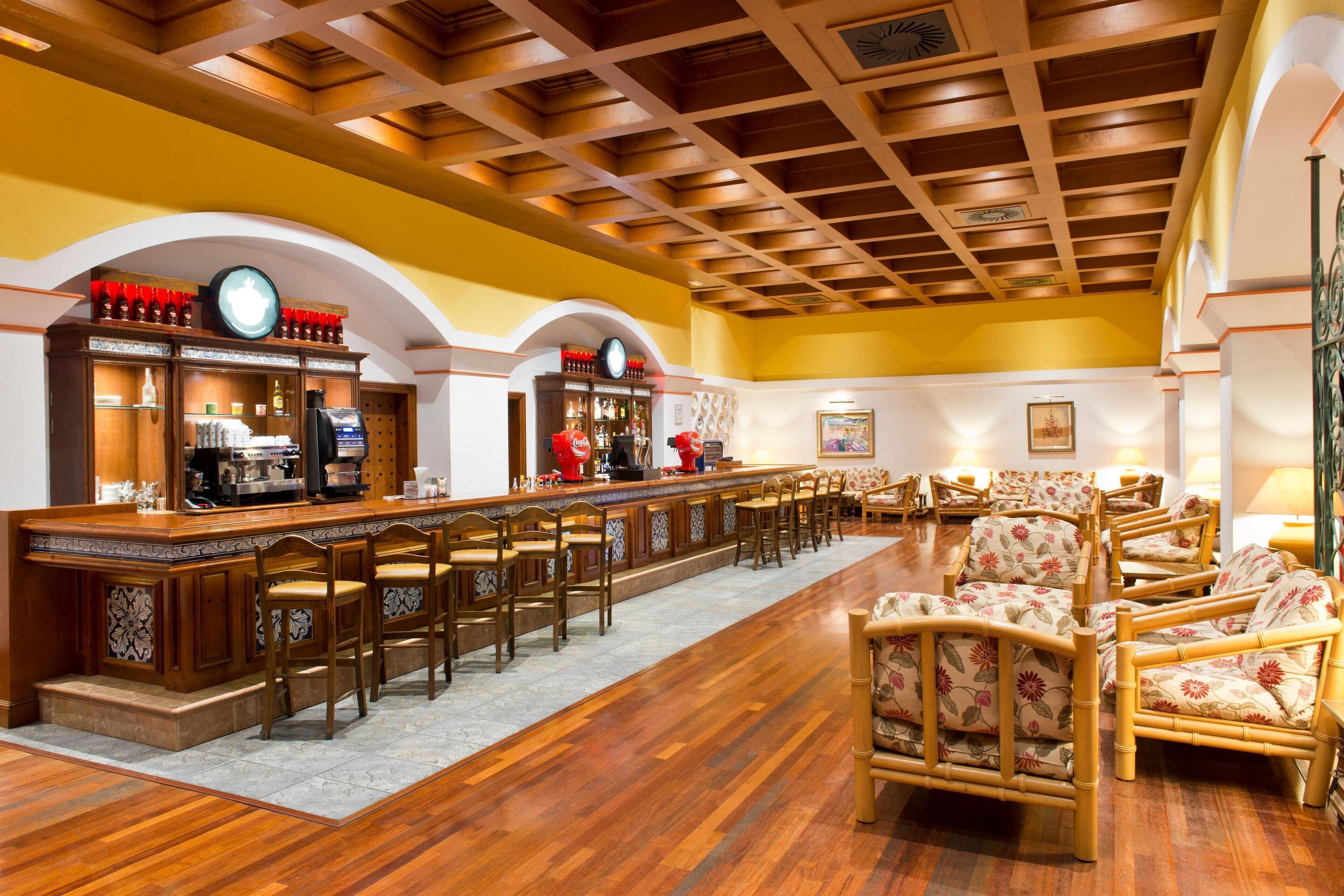 A bar area with wooden bar counters, multiple chairs, and a seating area with floral-patterned sofas.