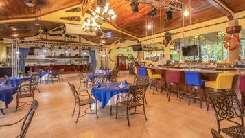 Un restaurante con varias mesas y sillas, una zona de bar y una cocina al fondo.