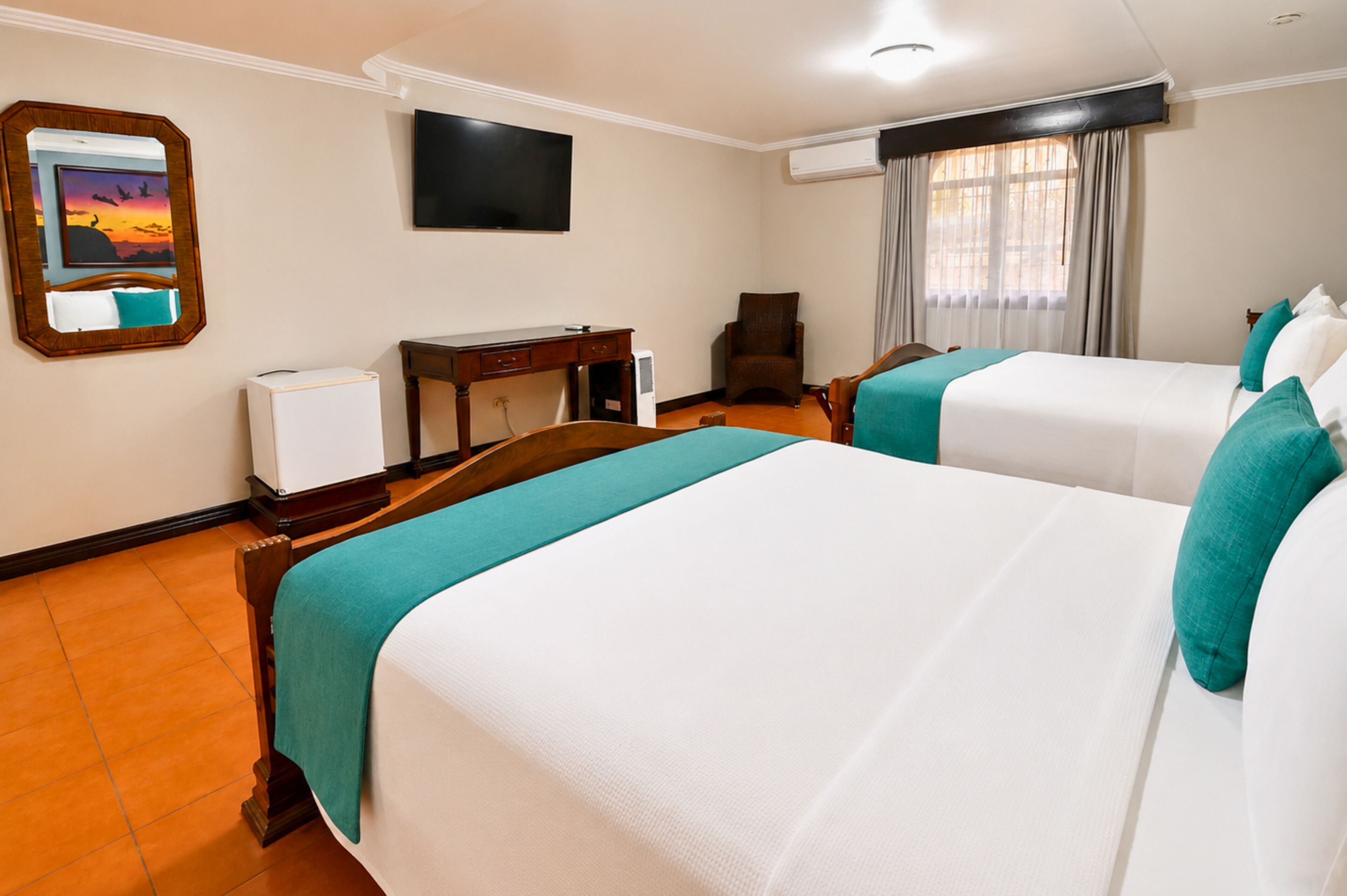 Habitación de hotel con dos camas, un escritorio, una silla, un televisor y una ventana con cortinas.