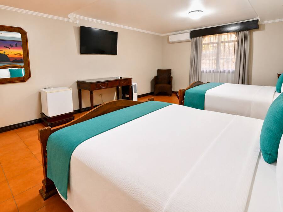 Habitación de hotel con dos camas, un escritorio, una silla, un televisor y una ventana con cortinas.