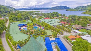 An aerial view of a resort with multiple swimming pools, a tennis court, and lush greenery surrounding the facilities.