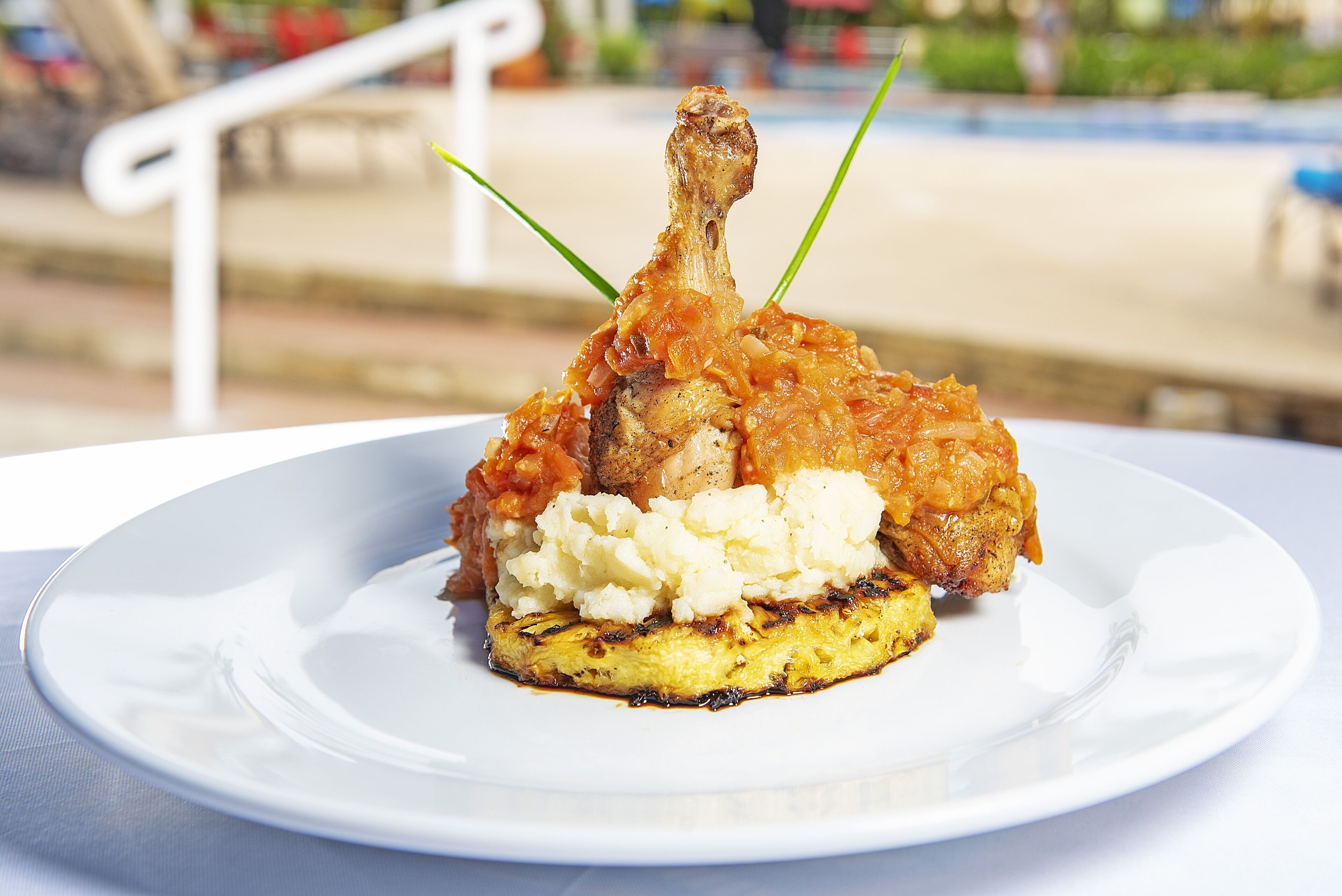 Une assiette comprenant un morceau de poulet grillé, de la purée de pommes de terre et une tranche d’ananas grillé.
