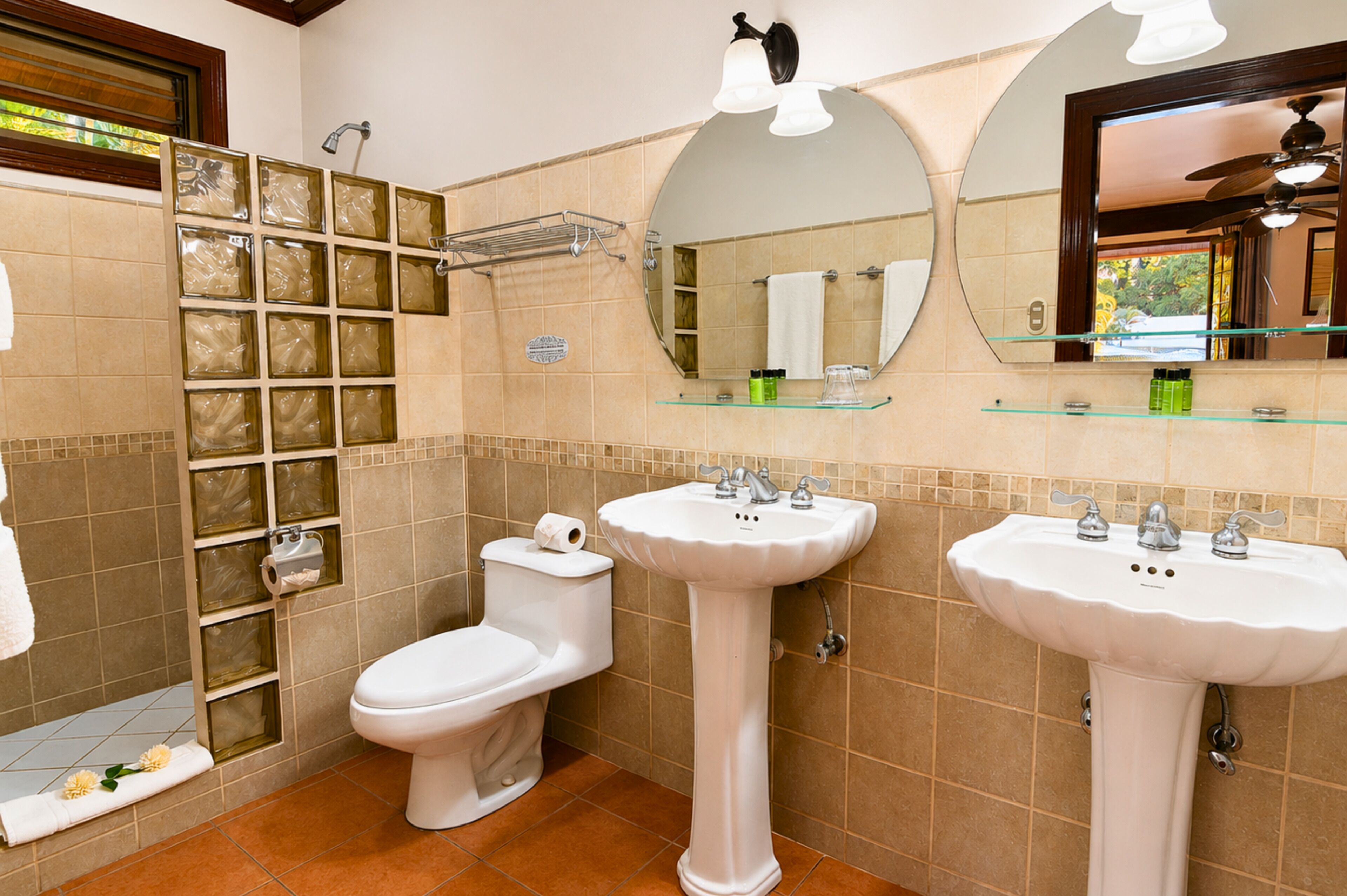 Baño con dos lavamanos, inodoro, ducha con puertas de vidrio y espejo sobre el lavamanos.